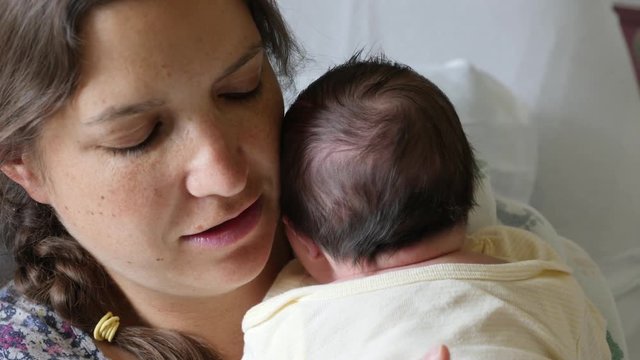 A tired mother burping a newborn girl after nursing her in the hospital