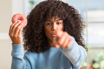 Fototapeta na wymiar African american woman holding donut at home pointing with finger to the camera and to you, hand sign, positive and confident gesture from the front
