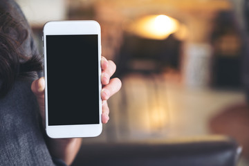 Mockup image of a woman holding and showing white mobile phone with blank black screen in cafe