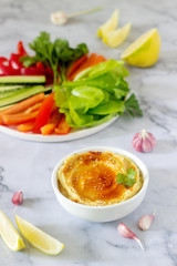 Hummus, different vegetables and lettuce leaves with lemon and garlic on a light background. Vegan food.