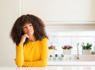 African american woman wearing yellow sweater at kitchen with hand on chin thinking about question,...
