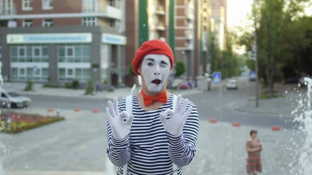 Mime in red beret and stripped shirt show two signs okey on camera