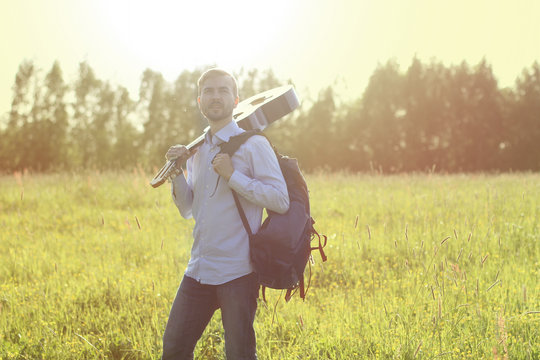 Man standing on the summer field with acoustic guitar and backpack. Summer travel concept