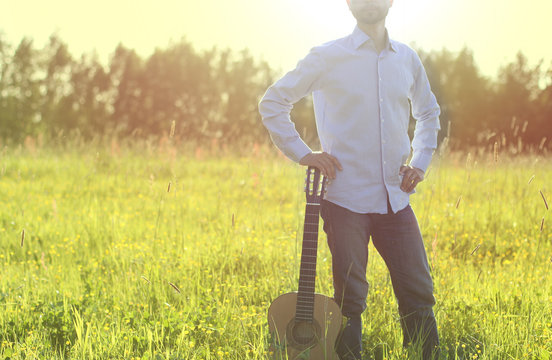 Man standing on the summer field and holding acoustic guitar. Copy space. Summer outdoor festival concept