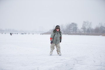 Fototapeta na wymiar A child on skates on a huge snow-covered lake. Skate on the river