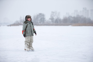 Fototapeta na wymiar A little boy in huge skates is riding on the lake.Entertainment on a winter day for a child.