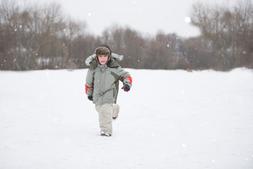 Fototapeta na wymiar A little boy runs through the snow in warm clothes and a hat with a fur hat.Child on a winter day