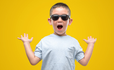 Dark haired little child wearing sunglasses very happy and excited, winner expression celebrating...