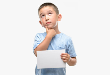 Dark haired little child holding a blank card serious face thinking about question, very confused...