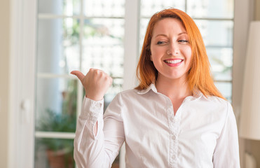 Redhead woman wearing white shirt at home pointing with hand and finger up with happy face smiling