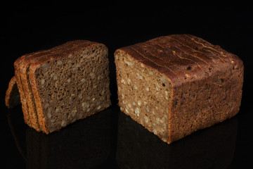 Ordinary bread with grains and sesame cut into pieces on a black background. Whole wheat bread