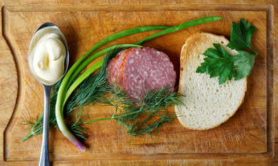 Sausage, greens, mayonnaise and a piece of bread lie on the table