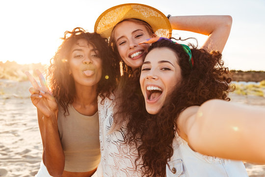 Fototapeta Three positive multiethnic women 20s in summer clothing smiling at camera, while taking selfie photo during holiday on nature