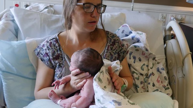 A tired mother burping her newborn girl after nursing her in the hospital