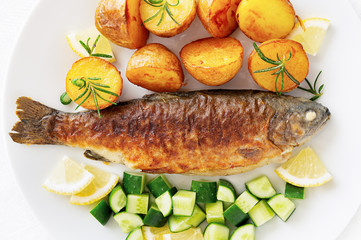 fried trout with young potatoes decorated with rosemary, cucumber salad, and lemon 