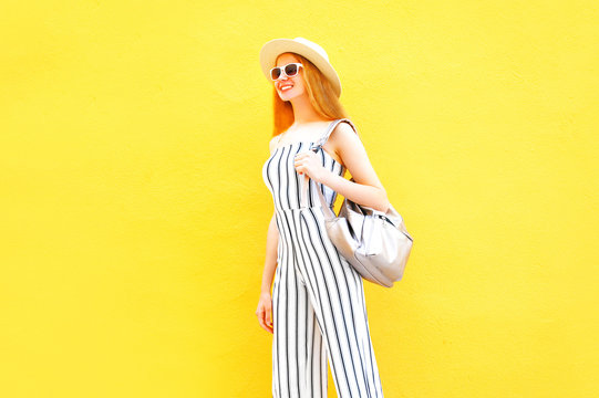 Fashion happy smiling woman in a white striped pants, round hat on a colorful yellow wall background