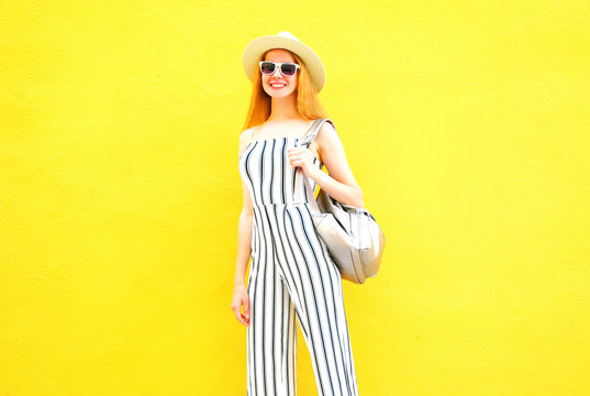 Fashion smiling woman in a white striped pants, round hat on a colorful yellow wall background