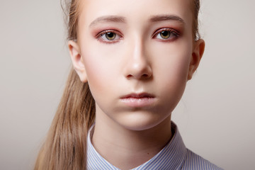 Portrait of a girl with professional makeup and in a blue shirt on a gray background close-up.