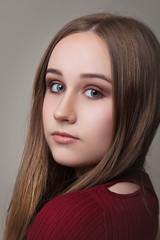 Fototapeta premium Portrait of brown-haired girl with long straight hair in a Burgundy dress and makeup on a gray background close-up.