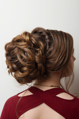 Wedding hairstyle bun on the head of brown-haired women on a gray background close-up rear vie
