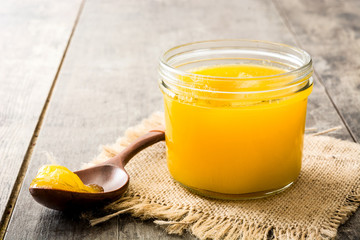 Ghee or clarified butter in jar and wooden spoon on wooden table. 