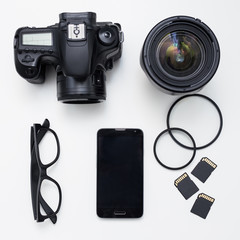 photographer's equipment - top view of camera, lenses, cards and smart phone over white table