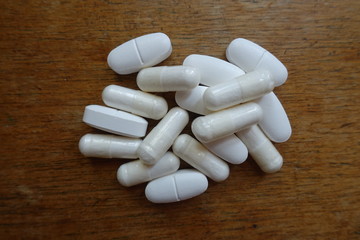 Fototapeta na wymiar Heap of white caplets of calcium citrate and capsules of magnesium citrate on wood