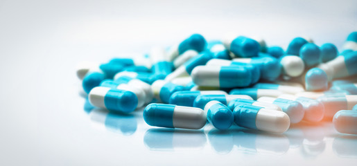 Selective focus on blue and white capsules pill spread on white background with shadow. Global...
