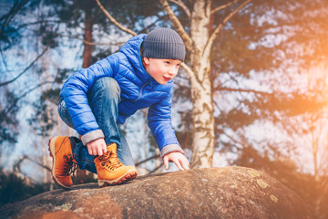 A young ranger in hiking boots climbs the rocks in search of adventure, discoverer and explorer