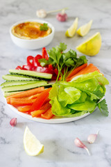 Hummus, different vegetables and lettuce leaves with lemon and garlic on a light background. Vegan food.