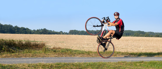 Cheerful cyclist riding on the rear wheel. Biker balancing while driving on a road bike. Risky ride...
