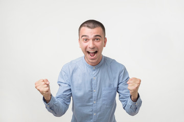 Fototapeta premium young hispanic man in blue shirt celebrating victory of his team over gray background