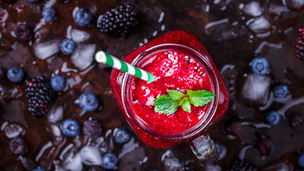 Smoothies.Drink Summer from Mix Berries Decorated with Green Mint. Compote in in a glass jar with a straw. Old dark Background. Superfoods and healthy lifestyle or detox diet food concept.