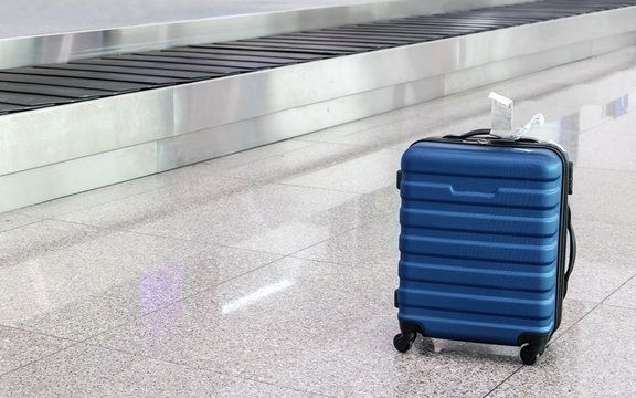 A forgotten lost suitcase in the airport hall. One case stands on wheels at the luggage transporter belt.