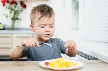 a child in a t-shirt in the kitchen eating an omelet, a fork