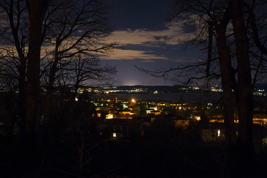 Panoramic view of a winter night sky with cloudy steps over cityscape with lake and hills.