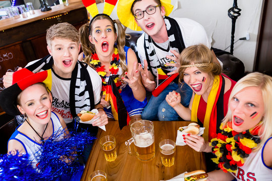 Football fans in sports bar watching a game with excitement wearing flags and make-up