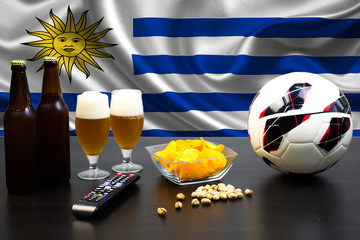2 bottles of beer, 2 glasses of beer next to the football on the background of the flag of Uruguay.