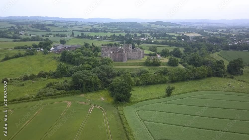 Sticker Aerial drone view flying towards the ruins of a medieval castle over green fields and farmland (Raglan Castle)