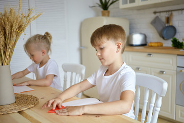 Handsome serious schoolboy and his little blonde brother sitting at wooden table and doing homework. Two brothers siblings reading at kitchen counter. Family, eduction, childhood and school