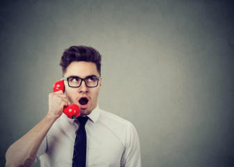 shocked young business man talking on a red telephone