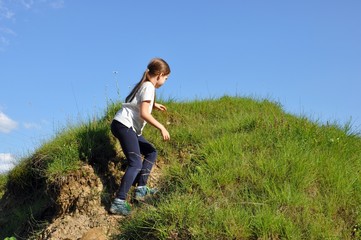 Child, blonde girl with long hair, climbing a little hill with green grass