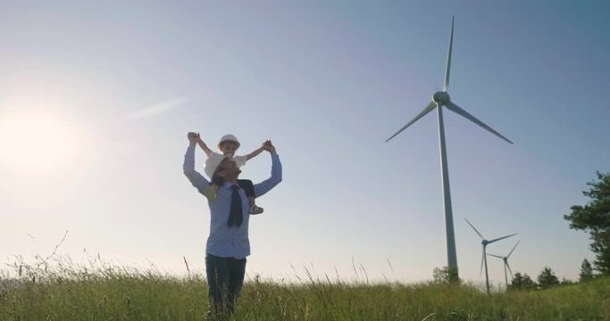 A father engineer holds his daughter in his arms and runs between the wind turbines with great freedom. Concept of: environmental engineering, renewable energy and love for nature and for the family