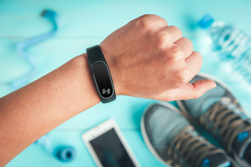 Fitness tracker on hand. Sneakers, bottle of water, tape measure on blue wooden background. Healthy lifestyle.
