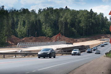 Fototapeta na wymiar Rural highway with cars. An excavator removing sand on a construction site. New road will be here. Central Ring Road moscow russia. Near Zvenigorod city