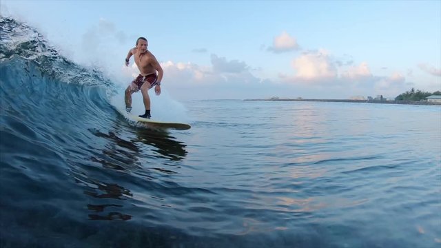 Amateur surfer rides glassy ocean wave on a fun surf board. Maldives