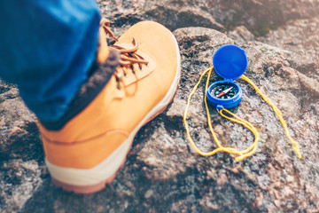 A close-up of the compass, the foot of a discoverer and a traveler in a walking boot on a rock, in search of adventures