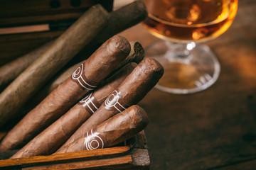 Cuban cigars closeup on wooden desk, blur glass of brandy - obrazy, fototapety, plakaty