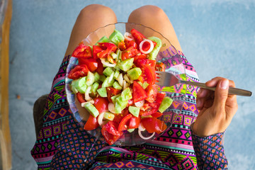 Woman hands holds on legs yummy vegetables tomato salad with onion rings, oil, garlic, spices on salad leaves garnished with raw sunflower seeds. Vegan vegetarian food concept. 