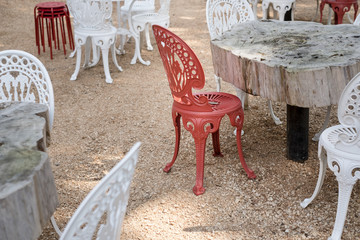 Red and white metal chairs and handmade tables made out of cut trees outdoors. Cozy vintage style waiting for guests in summer.
